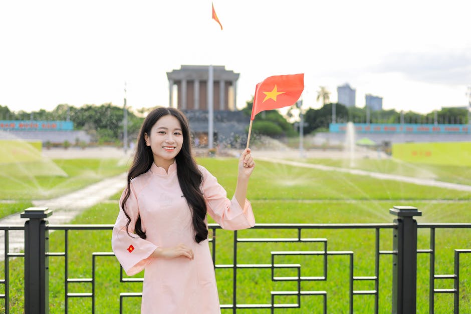 Young woman in traditional dress holding Vietnamese flag in front of a famous landmark in Hanoi.